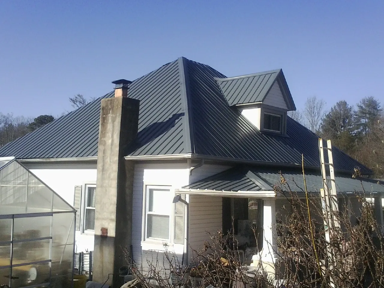 Dark blue standing seam metal roof on a white farmhouse with dormer — Slate & Tile Roof Repair by Roofing Brothers in New Albany