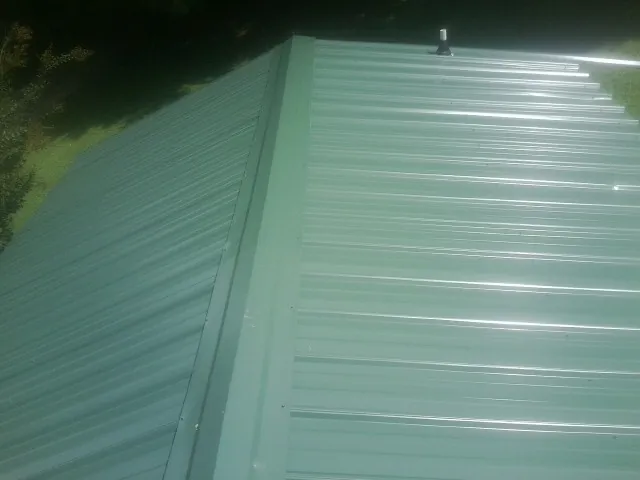 New green metal panels meeting at the ridge of a roof — Flat Roof Repair work by our crew in New Albany