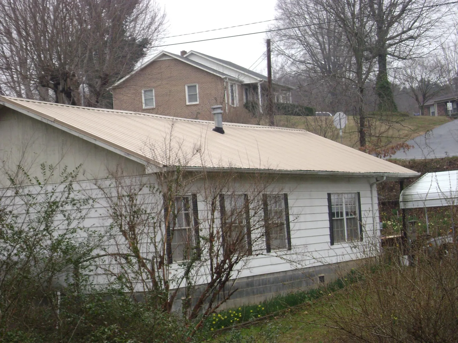 Tan metal roof on a white sided house set into a hillside — Commercial Roofing by Roofing Brothers in New Albany
